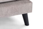 Close-up van een beige gestoffeerde meubelhoek met een donkere houten poot. De stof heeft een gestructureerde uitstraling en het ontwerp is modern en minimalistisch, tegen een witte achtergrond.