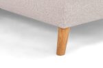 Close-up van een beige stoffen hoekbank met een enkele houten poot op een lichte achtergrond. De stof heeft een subtiel gestructureerd patroon en de poot is een gladde, natuurlijke houtafwerking, die contrasteert met de bekleding.