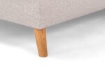 Close-up van een beige hoekbank met structuurstof en een enkele houten poot. De poot is taps toelopend en lichtbruin, en loopt door vanaf de onderkant van de bank, die op een wit oppervlak staat.