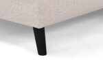 Close-up van een beige stoffen hoekbank met de structuurbekleding en één enkele zwarte houten poot op een witte achtergrond.