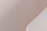 Close-up van een gestructureerd stoffen oppervlak met diagonale lijnen in beige en een witte hoek met fijne strepen. De stof creëert een subtiel patroon, wat suggereert dat het een zacht en comfortabel textielontwerp is.