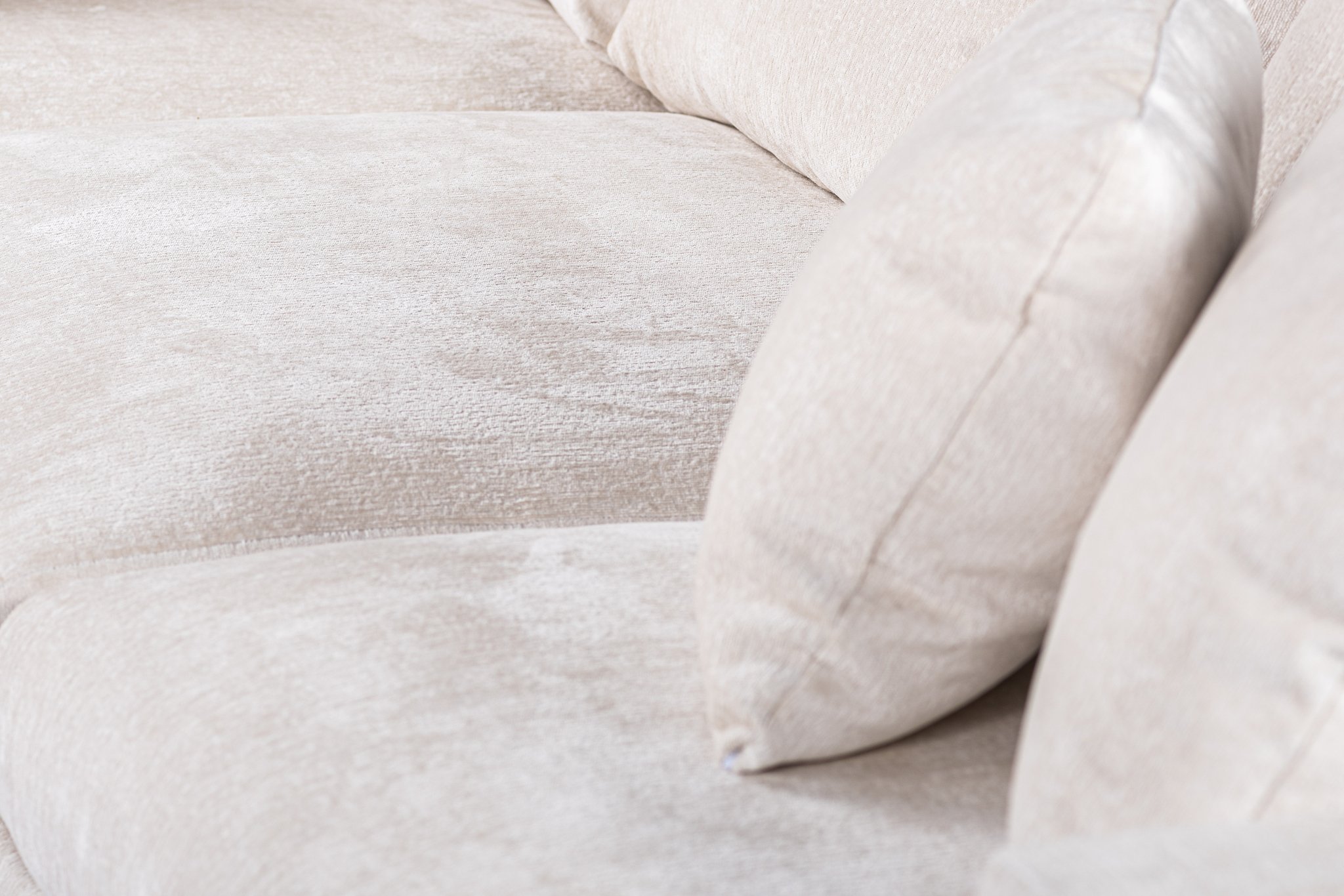 Close-up van een beige, getextureerde stoffen bank met een bijpassend kussen. De afbeelding benadrukt de zachte, comfortabele vulling en het zachte bekledingsmateriaal. De bank ziet er uitnodigend uit en is ideaal om te ontspannen.