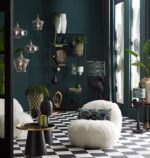 Een stijlvolle leefruimte met zwart-wit geblokte vloeren, pluche witte stoelen en een verscheidenheid aan planten. De kamer heeft hanglampen, een boekenplank met decoratieve items en grote ramen. Het decor combineert moderne en eclectische elementen.