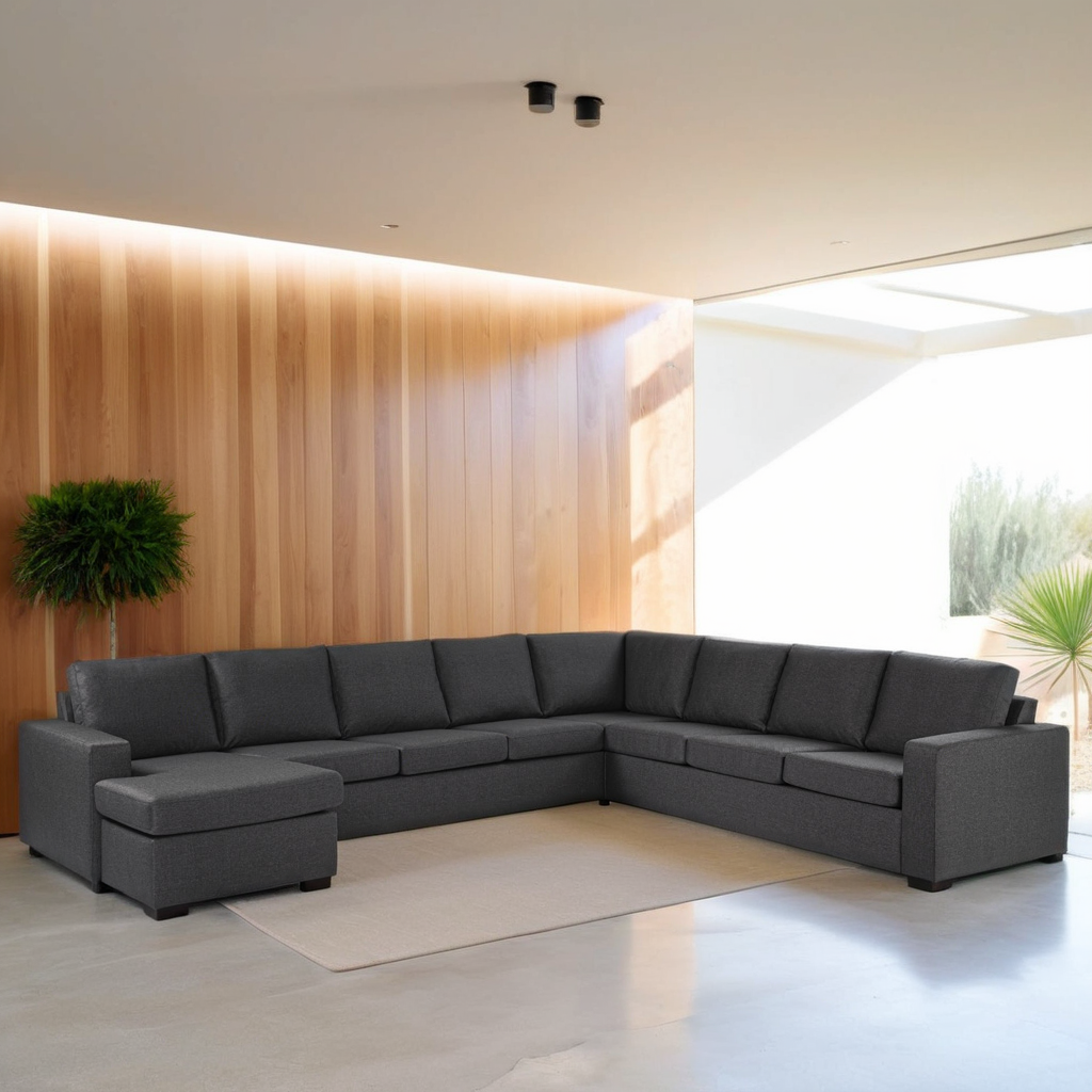 Een moderne woonkamer met een grote donkergrijze hoekbank in een L-vorm. De kamer heeft houten lambrisering, een wit kleed, een potplant en overvloedig natuurlijk licht dat door een dakraam stroomt. De vloer is lichtgekleurd en glad.