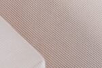 Close-up van een gestructureerd oppervlak met geribbelde strepen in een lichtbeige kleur. Een klein, gevouwen stukje witte stof met dunne, parallelle lijnen is zichtbaar in de hoek, gedeeltelijk overlappend met het beige materiaal.