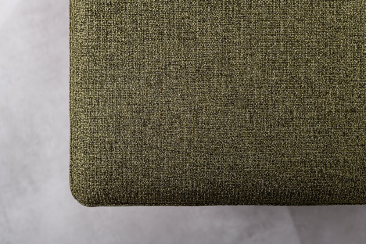 Een close-up van de 3 zits bank CL L+R, stof Dillon, D156 groen toont de olijfgroene gestructureerde bekleding tegen een lichtgrijze, subtiel gevlekte achtergrond.