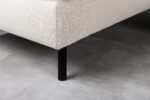 Close-up van de hoek van de 3 zits bank CL L+R in D820 ivoor stof Dillon, met zijn beige bekleding en eenvoudige zwarte cilindervormige poot, op een lichtgrijze tegelvloer.