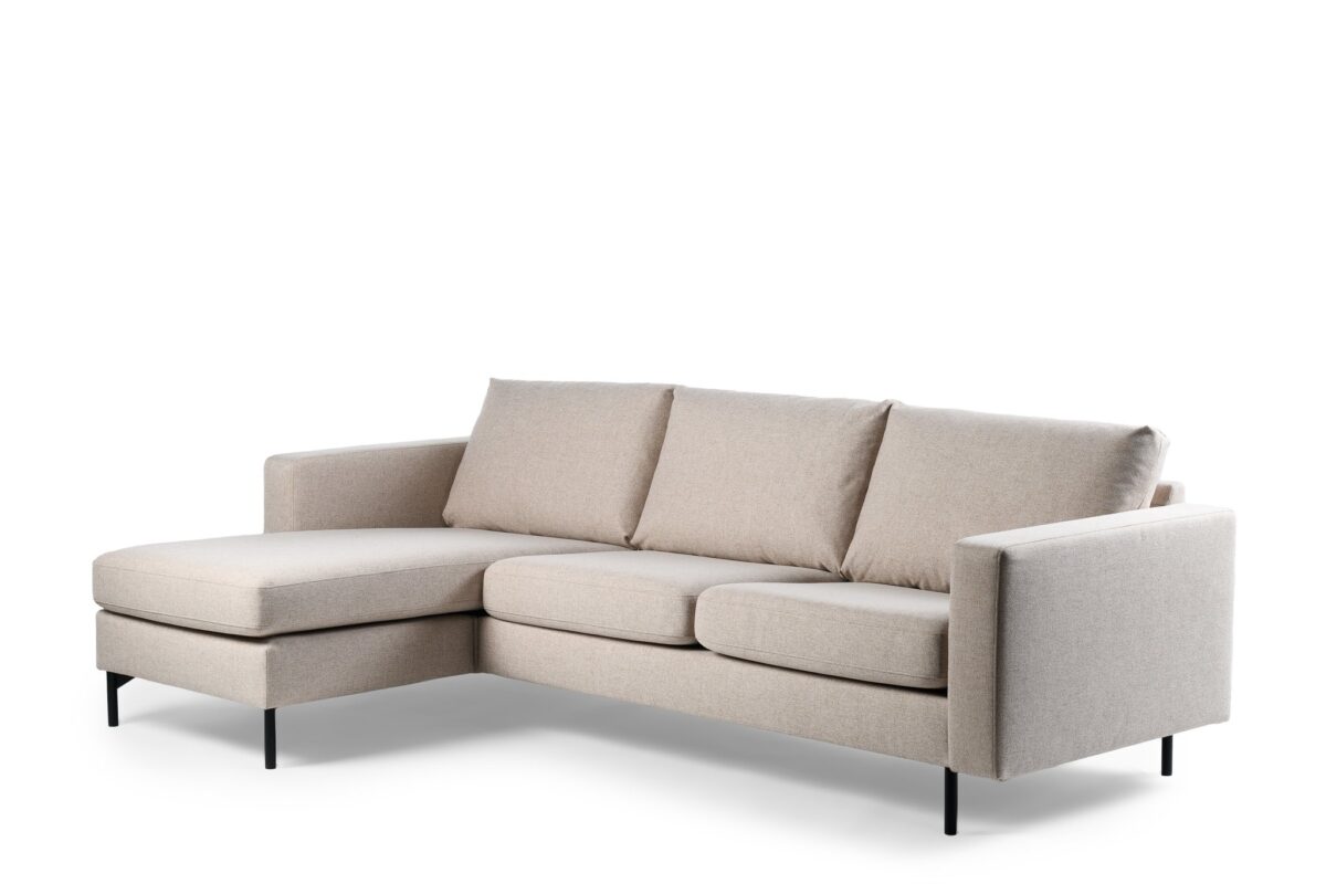 Een beige L-vormige sectionele bank met drie gewatteerde rugleuningen en een chaise longue aan de linkerkant. Het heeft strakke, minimalistische lijnen en wordt ondersteund door slanke zwarte metalen poten, tegen een witte achtergrond.