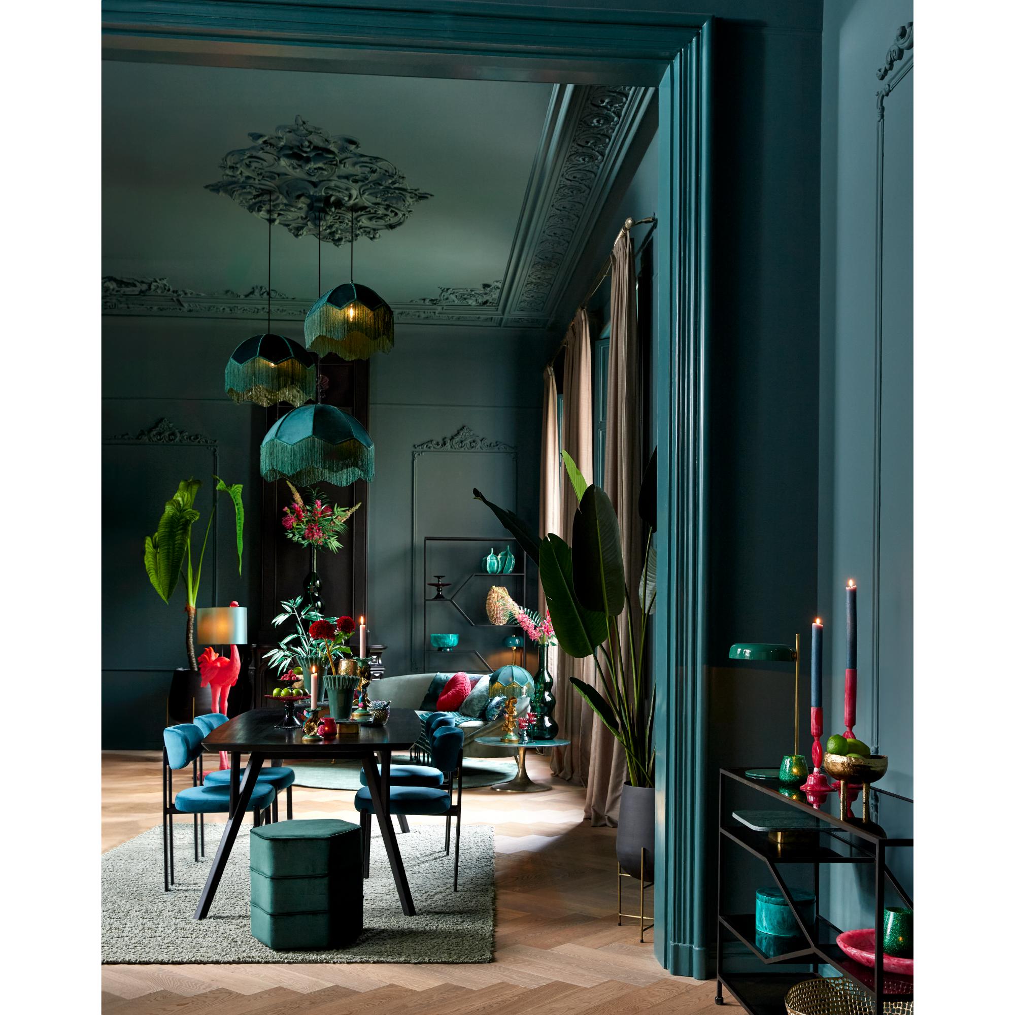 Luxe eetkamer met blauwgroene muren en plafond, sierlijke lijstwerk en meerdere hanglampen. Een donkere eettafel is omringd door stoelen, met weelderige groene planten en levendige decoratie die de ruimte accentueren. Kaarsen voegen warmte toe.