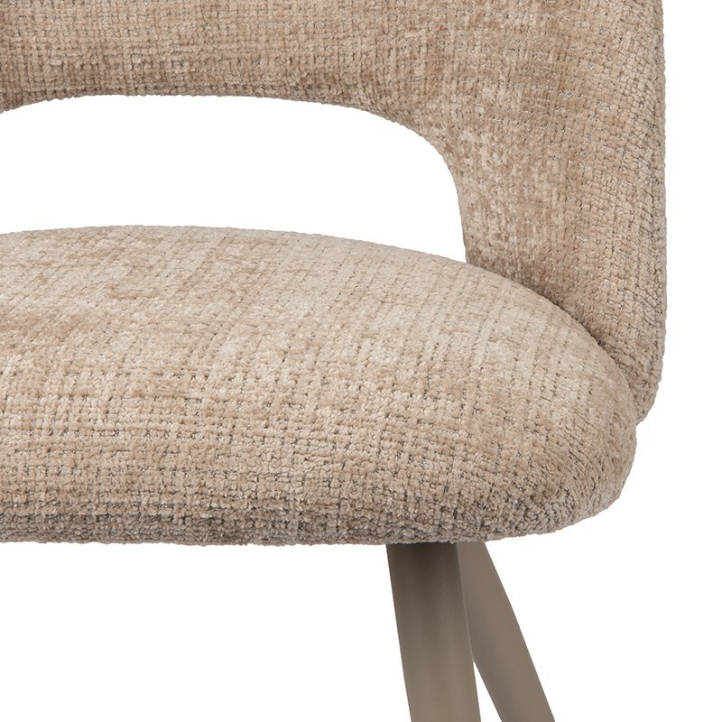 Close-up van een beige gestoffeerde stoel, met de gebogen rugleuning en zitting met een getextureerde stof. De stoel heeft dunne, lichtgekleurde poten. De achtergrond is effen wit.