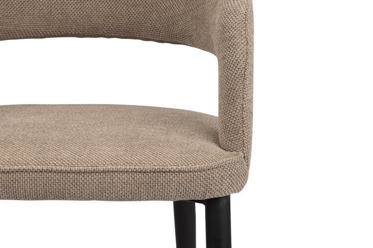 Close-up van een beige stoffen stoel met zwarte poten. De stoel heeft een gebogen rugleuning en een gewatteerde zitting, met een geweven structuurpatroon. De focus ligt op de bovenste en onderste delen van de stoel, tegen een witte achtergrond.
