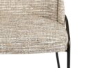 Close-up van een stoel met een gevlekt beige en bruin stoffen kussen. De stoel heeft zwarte metalen poten en een eenvoudig, modern design. Alleen een deel van de zitting en één poot zijn zichtbaar.