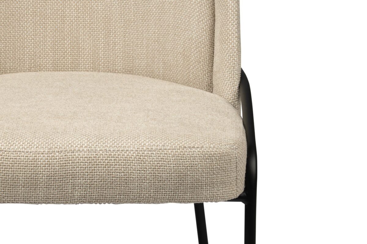 Close-up van een beige stoel met textuurstof en een gewatteerde zitting en rugleuning. De stoel heeft een strak zwart metalen frame, zichtbaar aan de zijkanten en poten.