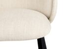 Close-up van een moderne stoel met een lichtbeige stoffen zitting en gebogen rugleuning. De stoel heeft strakke zwarte poten en een eenvoudig, elegant ontwerp. De textuur van de stof is zichtbaar, wat een gevoel van comfort toevoegt. De achtergrond is effen wit.