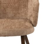 Close-up van een stoel van getextureerde beige stof met een houten poot. Het stoelontwerp heeft een gewatteerde, gebogen rugleuning en zitting, wat een gezellige en uitnodigende uitstraling creëert. De stof heeft een geweven patroon, wat visueel interessant is.