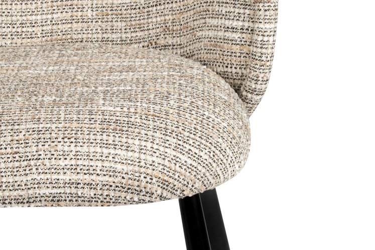 Close-up van een stoel met kussens en een getextureerde, beige en zwarte geweven stoffen bekleding. De stoel heeft houten poten die zwart geverfd zijn en slechts een deel van de stoel is zichtbaar. De achtergrond is effen wit.