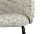 Close-up van een stoel met textuurstof met een gebogen rug en zitting in een gespikkeld patroon van crème, grijs en mosterdkleuren. De stoel heeft een zwarte metalen poot die zichtbaar is aan de onderkant.