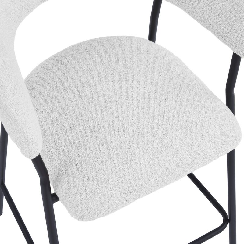 Een close-up van een stoel met een wit kussen met textuur en een zwart metalen frame. Het ontwerp heeft gebogen armleuningen en een eenvoudige, moderne esthetiek.