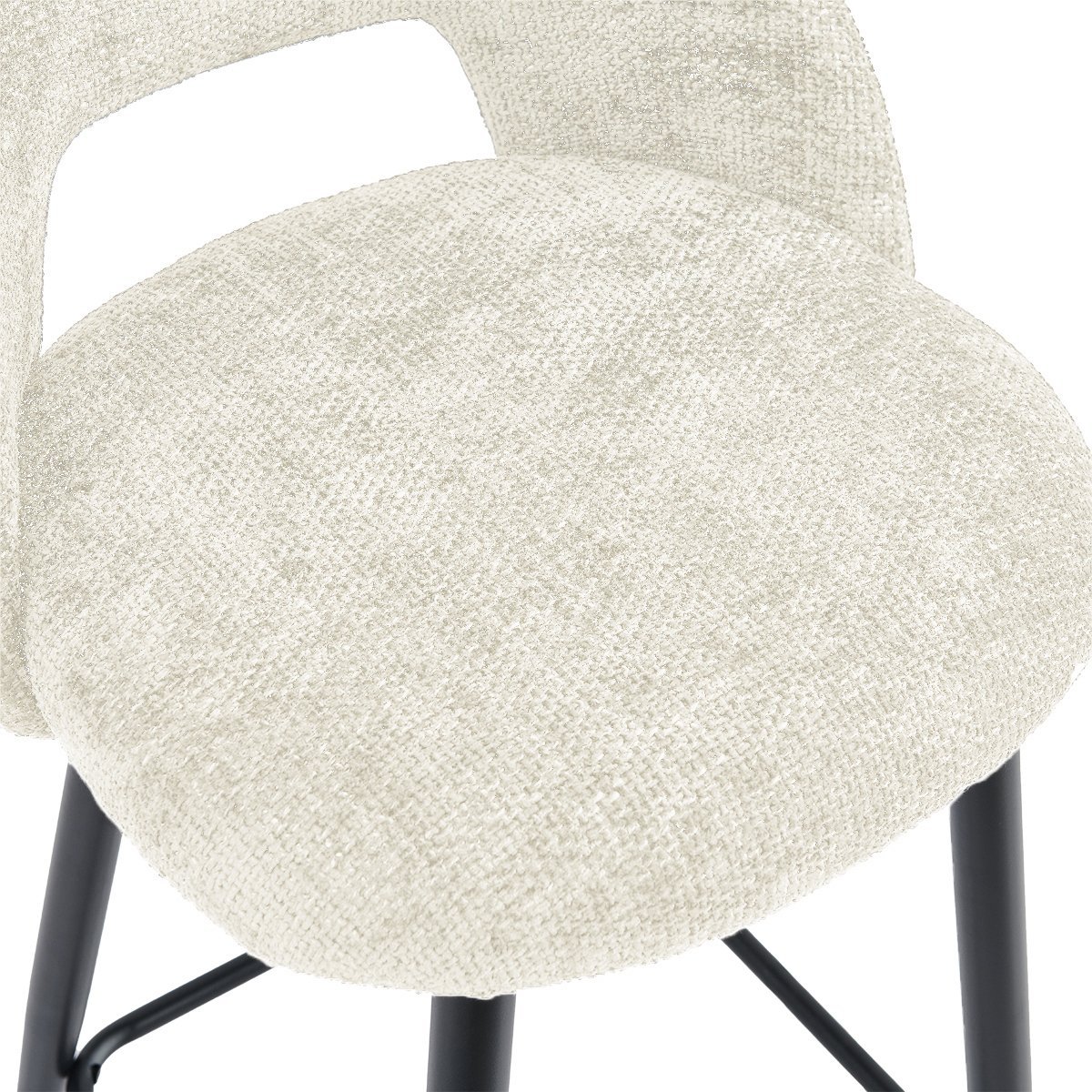 Close-up van een beige gestoffeerde barkruk met een getextureerd stoffen oppervlak. De kruk heeft een gebogen rugleuning met een uitsparing en wordt ondersteund door zwarte metalen poten.