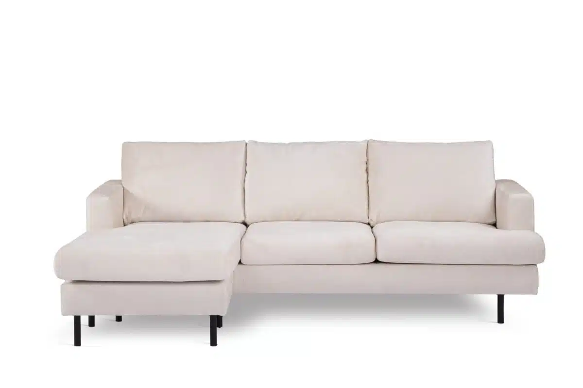 Een lichtbeige sectionele bank met drie kussens en een chaise longue aan de linkerkant. De bank heeft een minimalistisch design met zwarte poten, tegen een effen witte achtergrond.