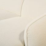 Close-up van een beige stoffen bank met de nadruk op de naad waar de armleuning de rugleuning raakt. De textuur van de bekleding is zichtbaar, wat een gevoel geeft van de zachtheid en kwaliteit van het materiaal.