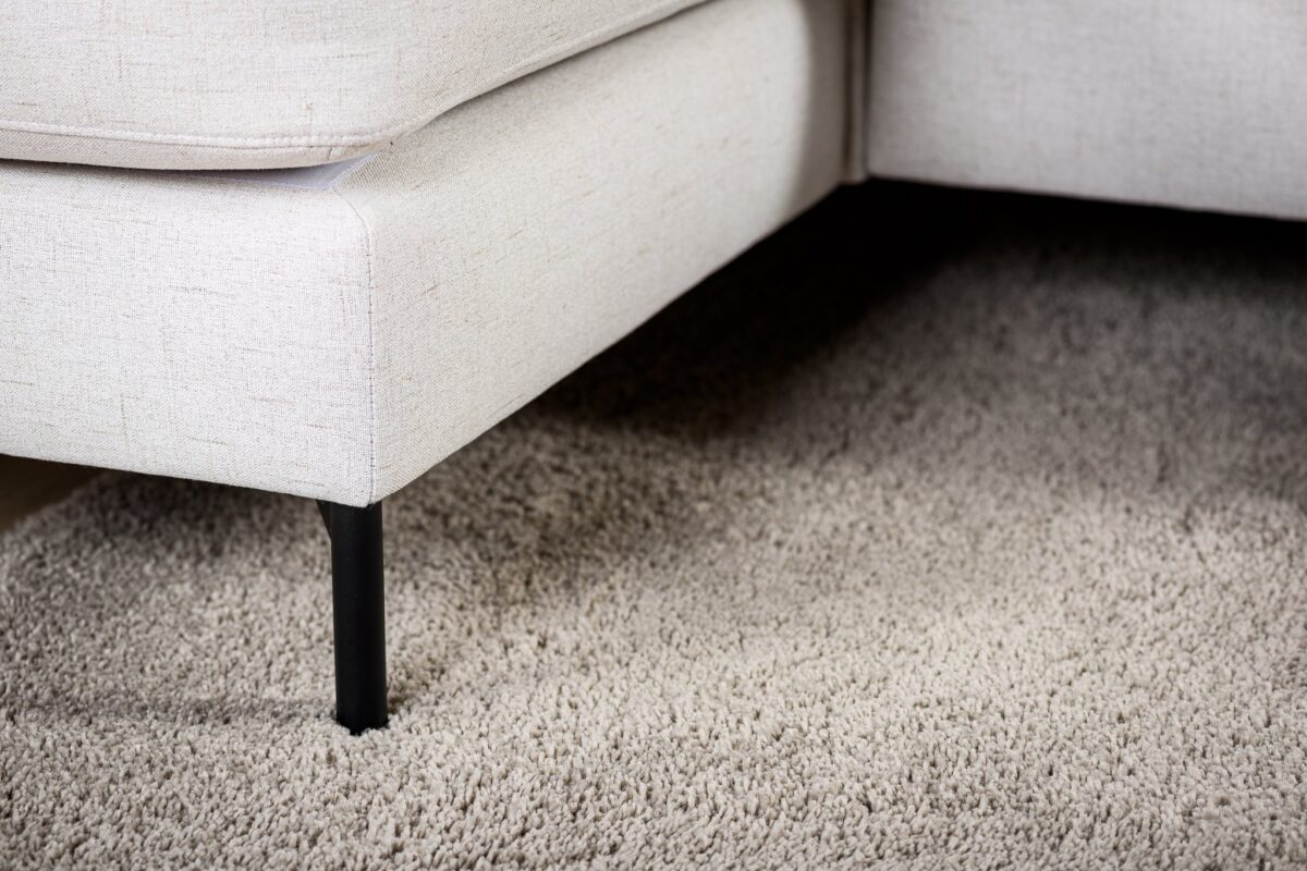 Close-up van de hoek van de 3 zits bank CL L+R in de stof Valente V920 naturel, met zwarte metalen poten op een beige getextureerd tapijt, waarbij de gedetailleerde bekleding van de bank en de zachtheid van het tapijt goed tot hun recht komen.