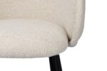 Close-up van een beige stoffen stoel met een gebogen rugleuning en zwarte poten, afgebeeld op een witte achtergrond. De stof heeft een getextureerde uitstraling, wat de zachtheid benadrukt.