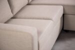 Close-up van een lichtbeige sectionele bank op een grijze vloer. De afbeelding richt zich op de hoek waar twee secties elkaar ontmoeten, waardoor de gladde, zachte stoffen bekleding en de zachte zitting worden benadrukt.