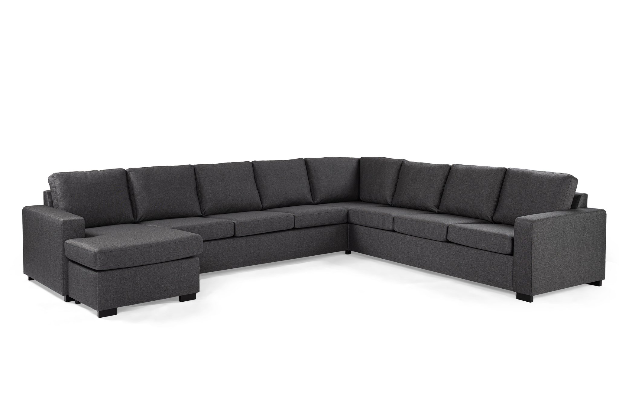 Een grote, donkergrijze sectionele bank met een chaise longue aan de linkerkant en gestoffeerde zittingen en rugleuningen. De bank heeft strakke, moderne lijnen en staat op korte zwarte poten. De bekleding lijkt van stof, wat het een comfortabele en uitnodigende uitstraling geeft.