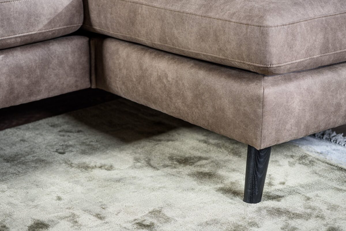 Close-up van de hoek van de 3 zits bank CL L+R in Savannah S520 taupe stof, met zwarte poten en geplaatst op een licht getextureerd vloerkleed.