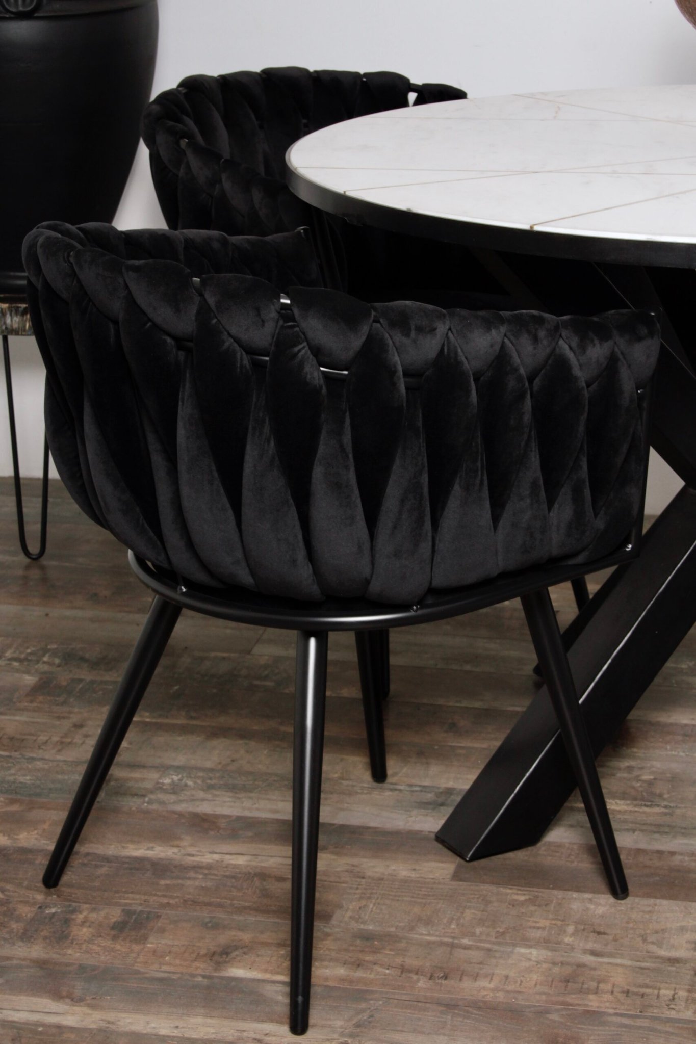 Een luxe zwarte fluwelen stoel met een gecapitonneerd patroon staat naast een ronde witte marmeren tafel. De stoel heeft strakke zwarte metalen poten en staat op een houten vloer in een moderne eetkamer.