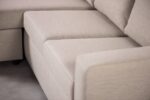 Close-up van een beige sectionele bank met strakke lijnen en zachte kussens, die een modern, minimalistisch design laat zien. De stof heeft een subtiele textuur en de armleuning van de bank is zichtbaar op de voorgrond.
