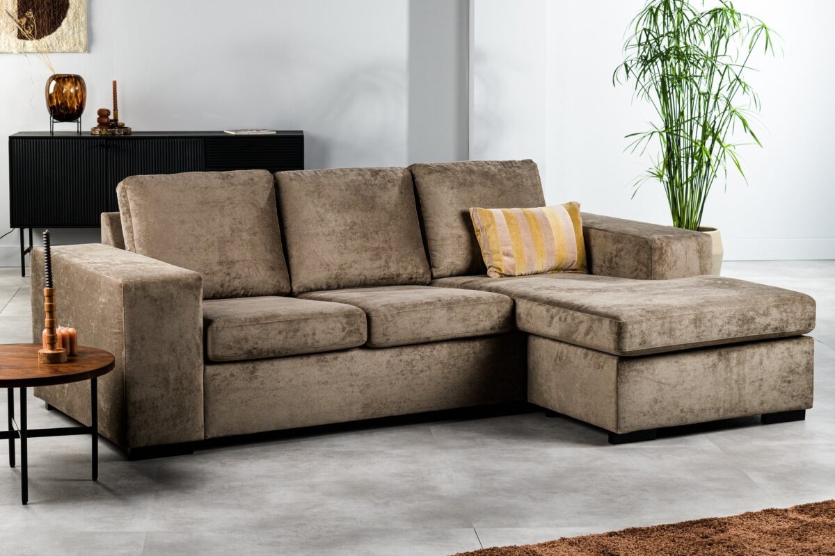 Een bruine 3-zitsbank, model CL L+R in de stof Hotel Chique (H430), staat in een moderne woonkamer met een geel gestreept kussen, chaise lounge, potplant, houten salontafel en zwart dressoir.