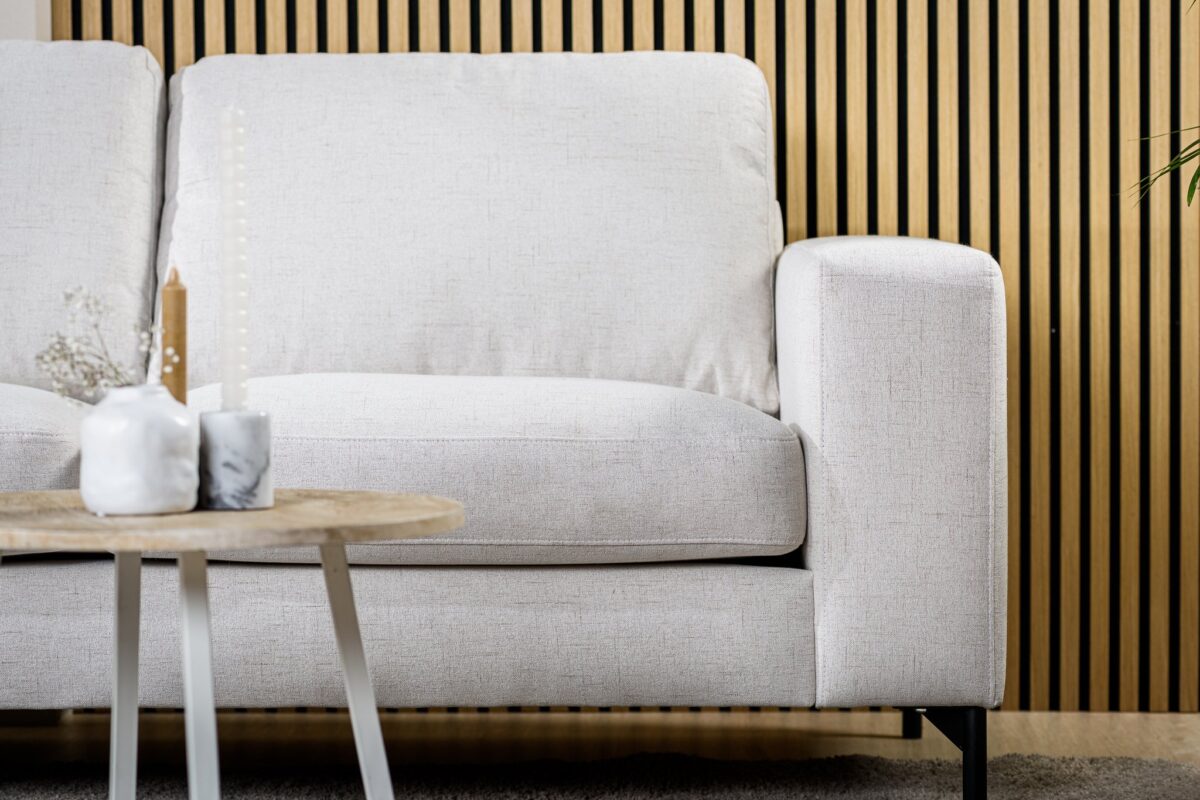 Een 3 zits bank CL L+R in Valente V920 naturel stof staat voor een houten latten wand, naast een kleine ronde tafel met minimalistische witte vazen en een bruine taper kaars.