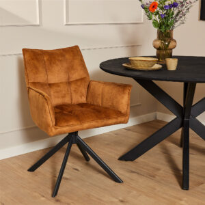 Moderne eethoek met de Eetkamerstoel Dani | Velvet Gold, een ronde zwarte tafel met een X-vormig onderstel en een vaas met kleurrijke bloemen, alles op een lichte houten vloer tegen een beige muur.