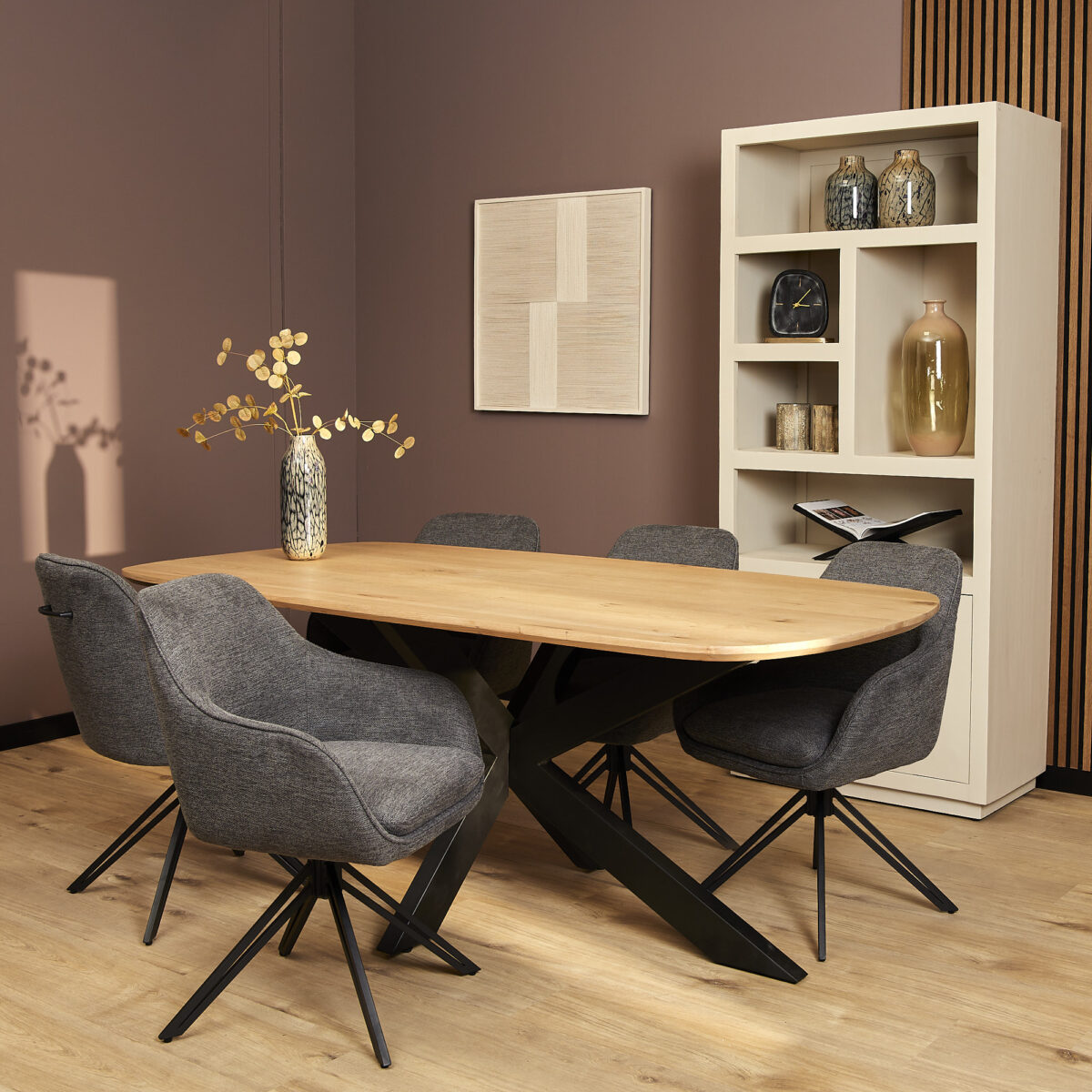 Moderne eethoek met een lichte houten tafel, zes Eetkamerstoel Jens | Antraciet stoelen, een vaas met takken en een witte plank met decoratie, tegen een gedempt paarse muur.