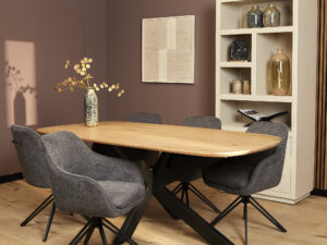 Moderne eethoek met een lichte houten tafel, zes Eetkamerstoel Jens | Antraciet stoelen, een vaas met takken en een witte plank met decoratie, tegen een gedempt paarse muur.