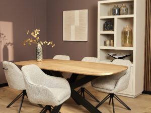 Moderne eetkamer met een lichte houten tafel, vijf Eetkamerstoel Jens | Beige stoelen, een hoge witte boekenkast met decoratie, geometrische wandkunst en een vaas met gouden takken op tafel.