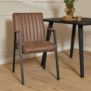 De Eetkamerstoel Tivoli met armleuning | Bull Brown met zwarte metalen poten staat naast een zwarte tafel met daarop een vaas, kom en mok op een lichte houten vloer in een moderne, minimalistische kamer.