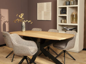 Moderne eetkamer met een houten tafel, zes Eetkamerstoel Jens | Bruine stoelen, een vaas met gedroogde bloemen en een lichte boekenkast met decoratie tegen een mauve muur en houten vloer.