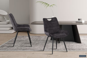 Twee 'Fancy' stoelen in zandkleurige stof (2 per doos) met metalen poten staan op een grijs vloerkleed in een stijlvolle, minimalistische kamer met een strakke tafel, een kleine camera, een vaas met plant en neutrale muren en vloer.