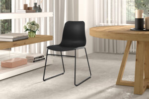 Een moderne, minimalistische kamer met Stoel 'Marie' PP Zwart stoelen (2 per doos) met metalen poten, een ronde houten tafel, witte planken met boeken, kaarsen en een vaas met bloemen bij grote ramen met vitrage.