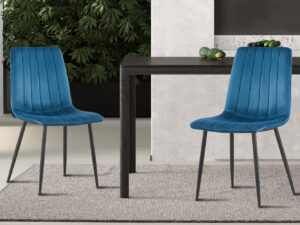 Twee moderne PROMO - Stoel 'Willis' Fluweel Blauw stoelen met zwarte poten staan rond een donkere, rechthoekige tafel op een licht tapijt, met groene bladplanten en een muur met marmereffect op de achtergrond.