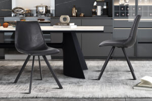 Twee Stoel 'Emma' PU Zwart stoelen (set van 2) staan op een grijs vloerkleed in een moderne keuken met donkere kasten, een marmeren achterwand en een eettafel versierd met boeken en decoraties.