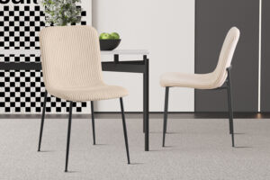 Twee Stoel 'Alice' Corduroy Beige stoelen (set van 2) met zwarte poten staan naast een witte tafel met groene appels erop, op een licht tapijt, in een moderne, minimalistische setting.