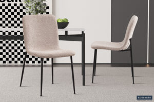 Twee Stoel 'Alice' Bouclé Beige stoelen (set van 2) met zwarte metalen poten staan rond een strakke witte tafel met groene appels in een neutraal gekleurde kamer met geometrische muurschilderingen.