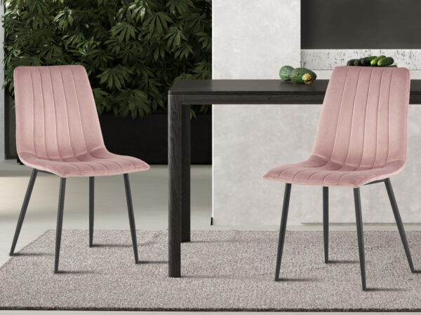 Twee roze fluwelen 'Willis' stoelen (Promo - Stoel 'Willis' Fluweel Roze) met zwarte poten staan naast een donkere houten tafel op een lichtgrijs kleed, met groene planten en een lichtgrijze muur op de achtergrond.