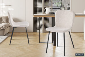 Twee Stoel 'Susan' Bouclé Zand stoelen (set van 2) met zwarte metalen poten staan naast een houten eettafel in een lichte, moderne keuken met visgraatvloer en neutrale inrichting.