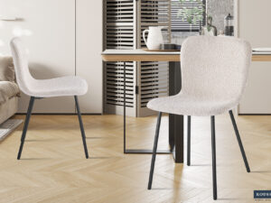 Twee Stoel 'Susan' Bouclé Zand stoelen (set van 2) met zwarte metalen poten staan naast een houten eettafel in een lichte, moderne keuken met visgraatvloer en neutrale inrichting.