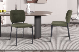 Twee PROMO - Stoel 'Sophia' Stof Groen stoelen met metalen poten omringen een moderne ovale tafel op een lichtgrijs vloerkleed in een eigentijdse kamer. De tafel staat vol met een witte vaas, appels en boeken.